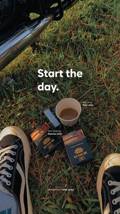 someone is standing on the grass with their feet up next to some books and a cup of coffee