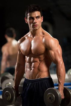 a shirtless man holding two dumbbells in his hands