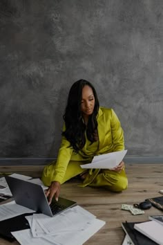 a woman sitting on the floor surrounded by papers and laptops looking at her computer