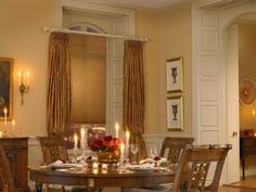 a dinning room table with candles and flowers on it in front of two windows