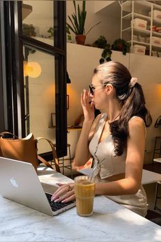 a woman sitting at a table with a laptop computer in front of her, drinking coffee