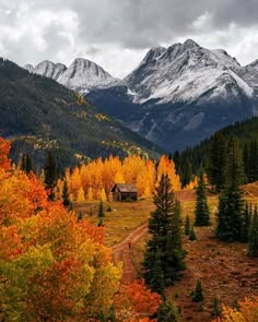 a cabin in the mountains surrounded by trees with yellow and red leaves on it's branches