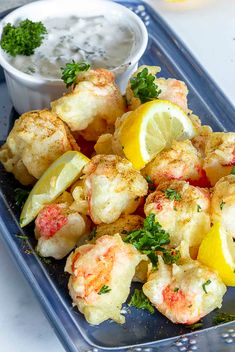 there is a blue tray with shrimp and lemons on it next to a small bowl of dipping sauce