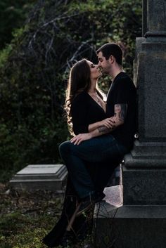 a man and woman sitting next to each other on a grave in the grass with trees behind them