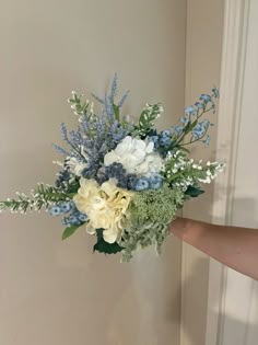 a bouquet of white and blue flowers is held up by someone's hand in front of a door