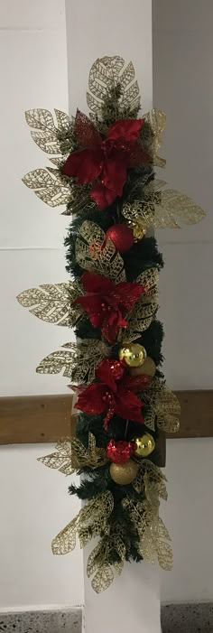 a christmas tree decorated with red and gold ornaments on top of a white pillar in a room