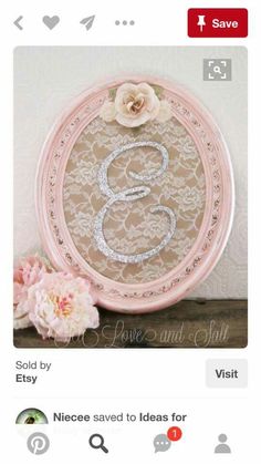 a pink frame with a white lace monogram on it and a flower in the middle