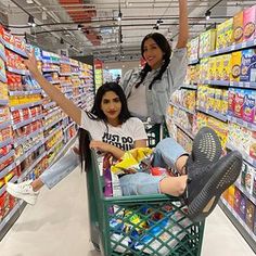 two women are sitting in a grocery cart and waving at the camera while another woman stands behind them