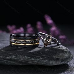 two rings sitting on top of a rock with purple flowers in the background and one is black