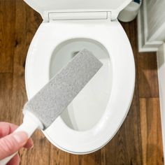 a person is using a toilet brush to clean the seat lid on a white toilet