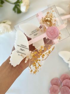 a person's hand holding a pink and white box with gold flakes on it