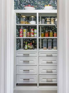 an organized pantry with white drawers and wallpaper