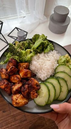 someone holding a plate with chicken, rice and cucumbers