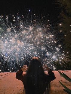 a woman sitting in front of a firework display with her back to the camera