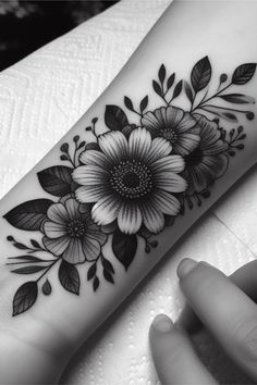 a black and white tattoo with flowers on the forearm, hand and wrist tattoos for women