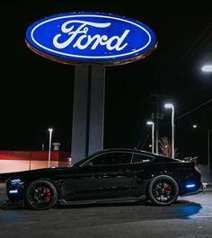 a black sports car parked in front of a ford dealership sign at night time