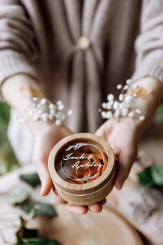 a person holding a wooden container with some writing on it and flowers in the background