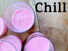 four glasses filled with pink liquid sitting on top of a wooden table