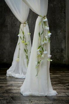 two white drapes with flowers and greenery hanging from the top, on a stone floor