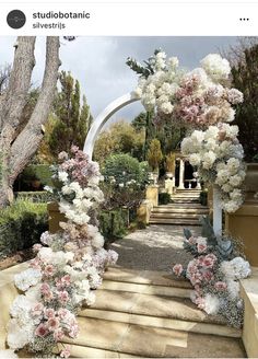 an outdoor wedding ceremony with flowers on the steps and archway in the background, surrounded by trees