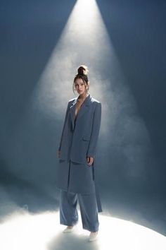 a woman standing in front of a spotlight on a blue background wearing a gray suit