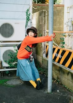 a boy in an orange shirt leaning against a pole