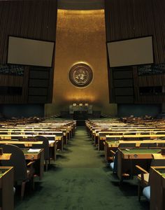 an empty room with rows of desks in front of the united states seal on the wall