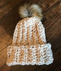 a crocheted beanie with a fur pom on top sitting on a wooden floor