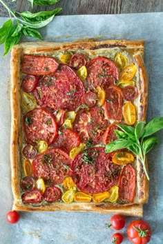 a square tart with tomatoes and basil on top, next to some fresh herbs