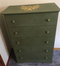 a green chest of drawers with an emblem painted on the top and bottom, sitting in a corner