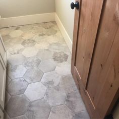 a bathroom with white and gray tile floors next to a wooden door, in front of a window