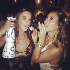 two beautiful young women standing next to each other eating food and drinking wine at a party