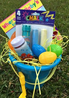 a blue bucket filled with baby items on top of a grass covered field next to a book