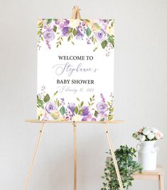 a welcome sign with flowers on it next to a potted plant and a wooden easer