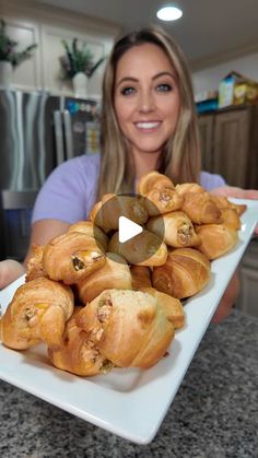 a woman holding a white plate filled with croissants on top of a counter