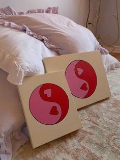 two pieces of artwork sitting on top of a bed next to pillows and pillow cases