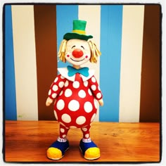 a close up of a toy clown on a wooden table with striped wall in the background