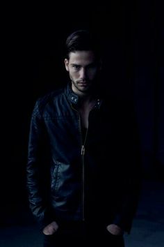 a man standing in the dark with his hands on his hips wearing a leather jacket