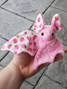 a hand holding a pink stuffed animal with strawberry print on it's wings and ears