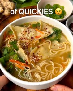 a bowl of soup with noodles, carrots and spinach in it on a wooden table