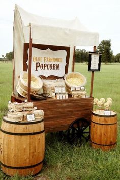 an old fashioned popcorn stand in the middle of a field with buckets full of popcorn