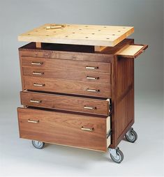 a wooden box on wheels with three drawers and one top drawer open to show the contents