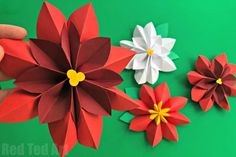 someone is holding some paper flowers on a green surface with red, white and yellow petals