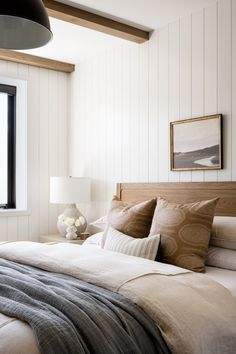 a large bed sitting under a window next to a lamp on top of a table