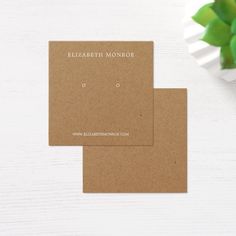 two brown business cards sitting on top of a white table next to a green plant