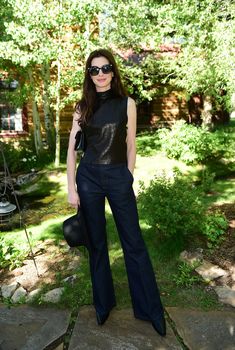 a woman standing on top of a stone walkway wearing black pants and a leather shirt