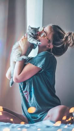 a woman holding a cat in her arms while sitting on a bed with candles around her