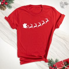 a red t - shirt with santa's sleigh on it next to presents