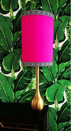 a pink lamp sitting on top of a table next to a green plant wallpaper