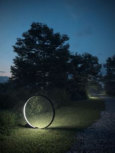 a light sculpture in the middle of a grassy area at night with trees and bushes behind it